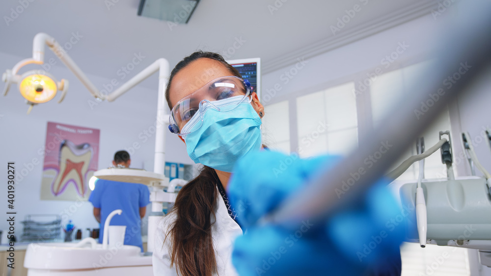 Fototapeta premium Patient pov to doctor in stomatological office treating teeth of woman. Orthodontic specialist and man assistant working wearing masks and gloves in modern dental clinic.