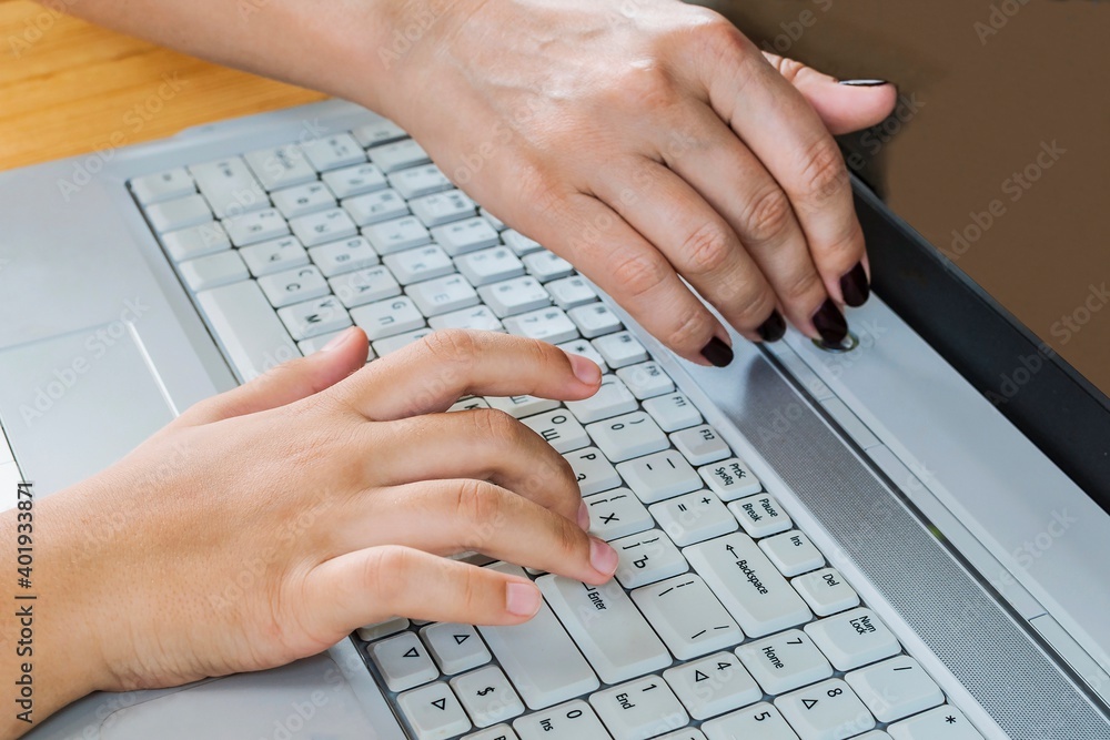 Control over the work of a teenager on the computer. The finger of a woman's hand on the laptop's power-off button. Control over the work of a teenager on the computer. The finger of a woman's hand on the laptop's power-off button.