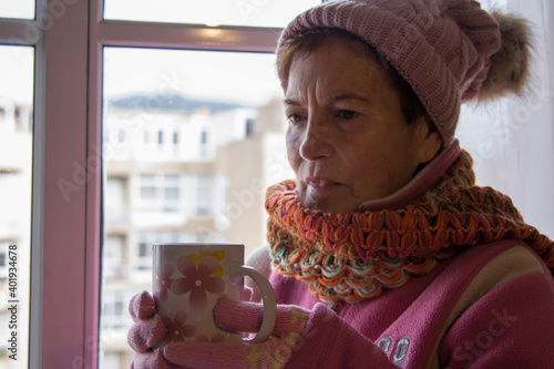 warm senior woman looking out the window and having a cup of coffee