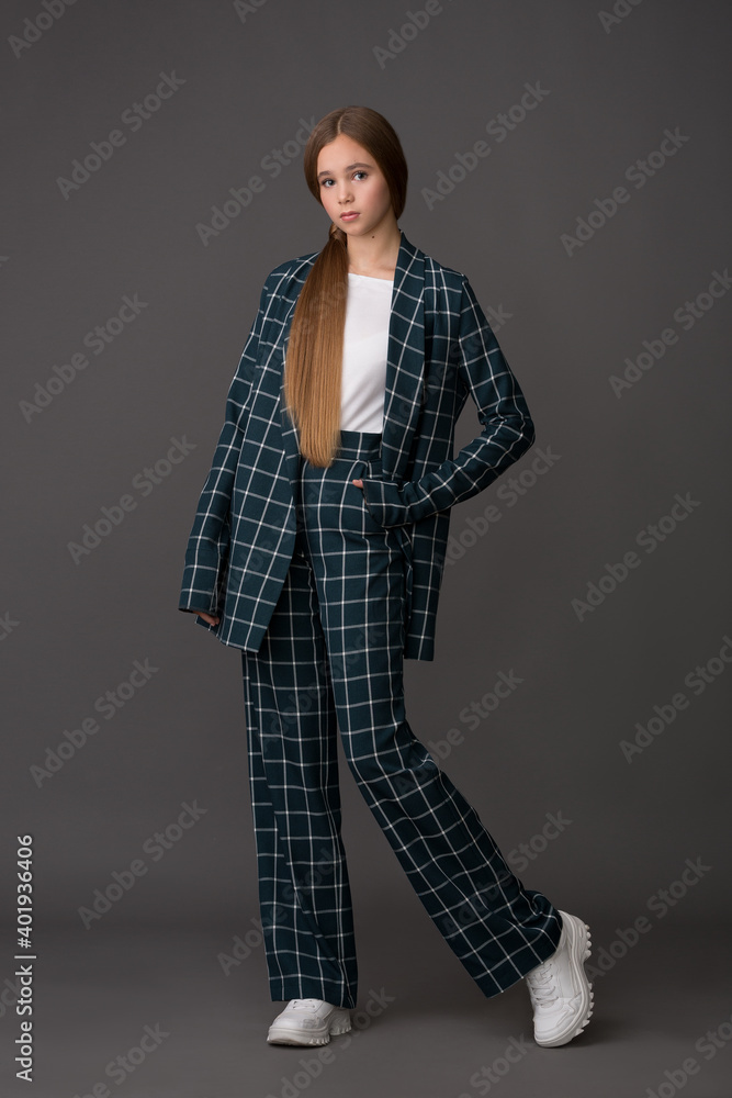 beautiful girl teenager blonde with long hair in a stylish suit in a cage posing in the studio on a gray background beautiful girl teenager blonde with long hair in a stylish suit in a cage posing in the studio on a gray background