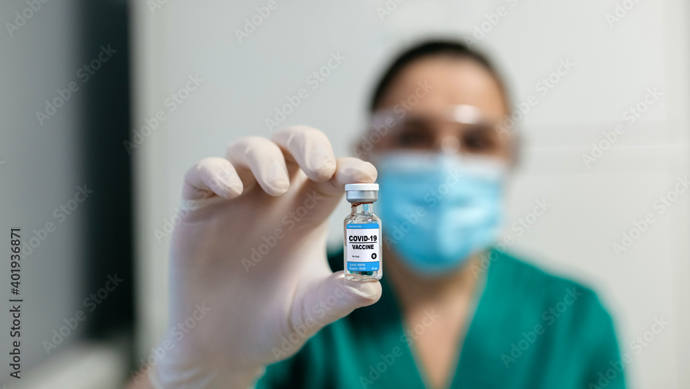 Unrecognizable female laboratory technician showing vial of coronavirus vaccine. Selective focus on vial in foreground Unrecognizable female laboratory technician showing vial of coronavirus vaccine. Selective focus on vial in foreground