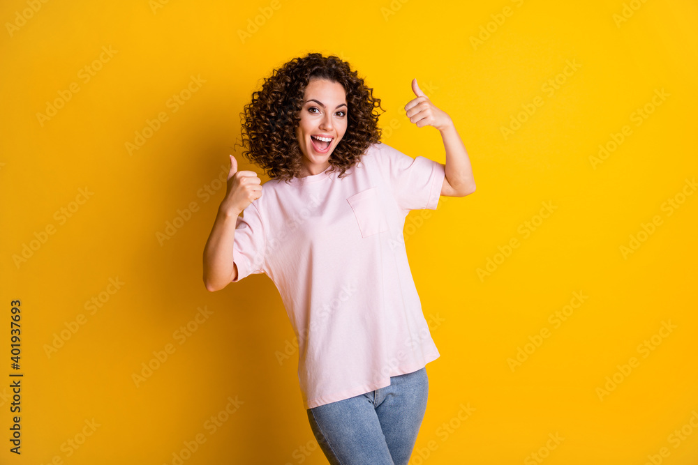 Photo portrait of happy girl raising two thumbs up isolated on vivid yellow colored background