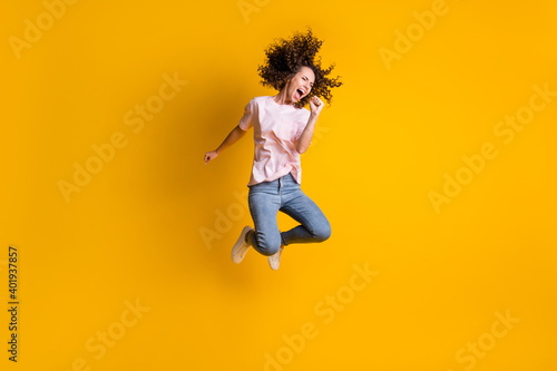 Photo portrait full body view of girl screaming into imaginary microphone jumping up isolated on vivid yellow colored background