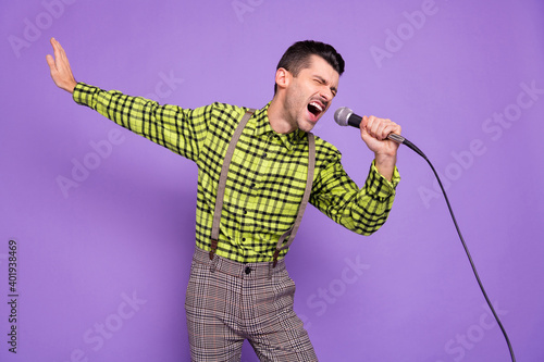 Photo of young crazy handsome man in checkered shirt and suspenders sing karaoke isolated on purple color background photo