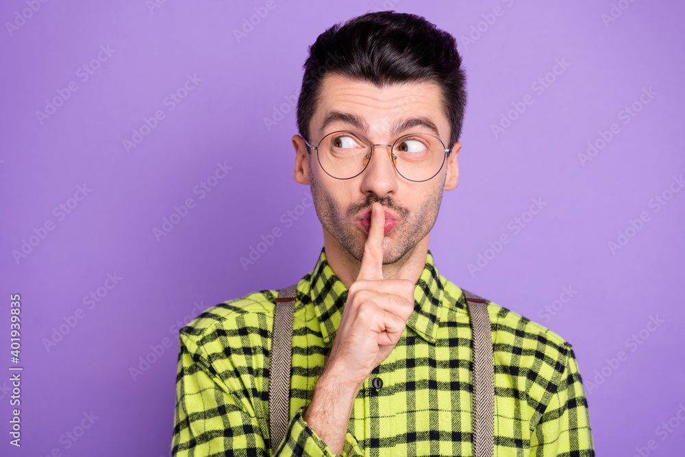 Photo portrait of man keeping secret closing lips with finger looking at blank space isolated on vivid violet colored background Photo portrait of man keeping secret closing lips with finger looking at blank space isolated on vivid violet colored background