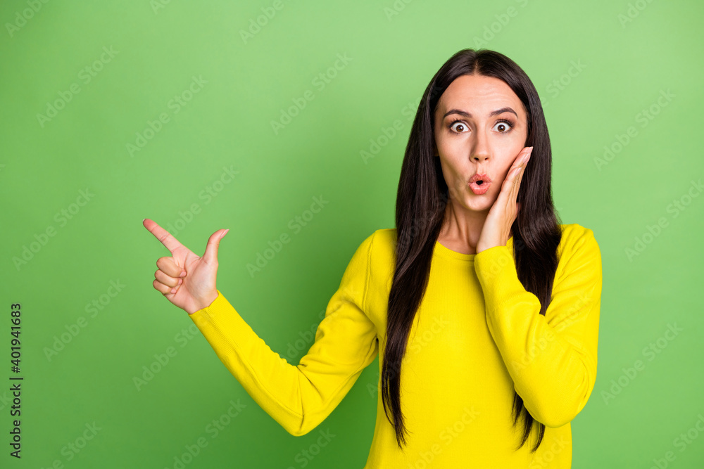 Photo of shocked person staring hand on cheek direct finger empty space proposition isolated on green color background Photo of shocked person staring hand on cheek direct finger empty space proposition isolated on green color background