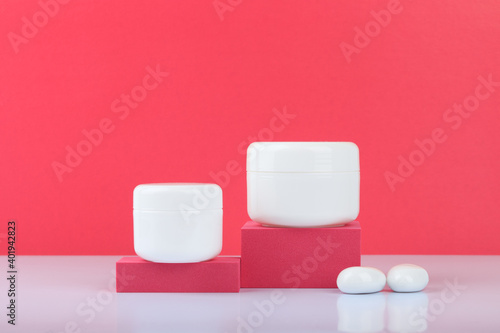 White cream jars on podiums against pink background with space for text. Concept of beauty and skin care
