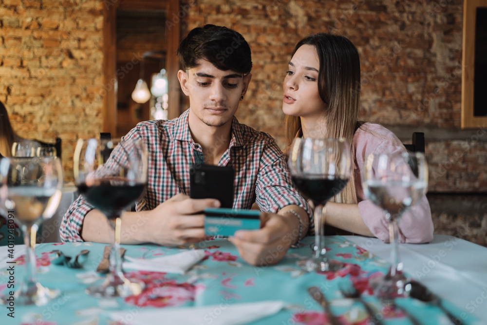 Fototapeta premium Young smiling couple shopping online together - Happy couple enjoying dinner and paying the bill with a credit card