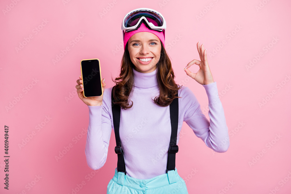Photo portrait of girl showing ok-sign holding phone with blank space display in one hand isolated on pastel pink colored background Photo portrait of girl showing ok-sign holding phone with blank space display in one hand isolated on pastel pink colored background