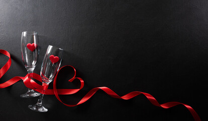 Valentine's day and love concept made from champagne glasses and red hearts on black wooden background. Top view with copy space, flat lay.