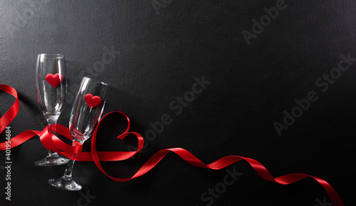 Valentine's day and love concept made from champagne glasses and red hearts on black wooden background. Top view with copy space, flat lay.