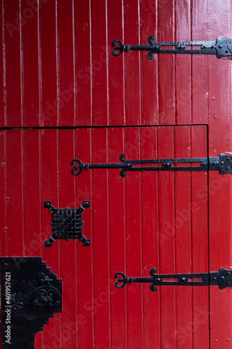 Partial view of a 16th century red castle door decorated with black ornaments for the hinges, the spy hole and for the lock photo