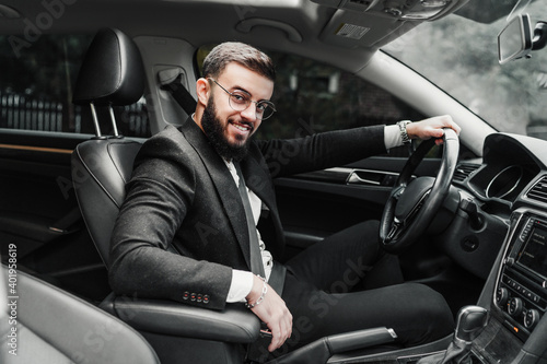 Portrait of a handsome elegant man in a suit sitting behind the wheel and looking at the camera with a smile. © Тарас Нагирняк