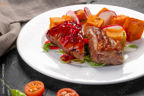 grilled farm duck breast with baked sweet potatoes and sweet lingonberry sauce. Tareka white on a dark background. For the restaurant menu. photo