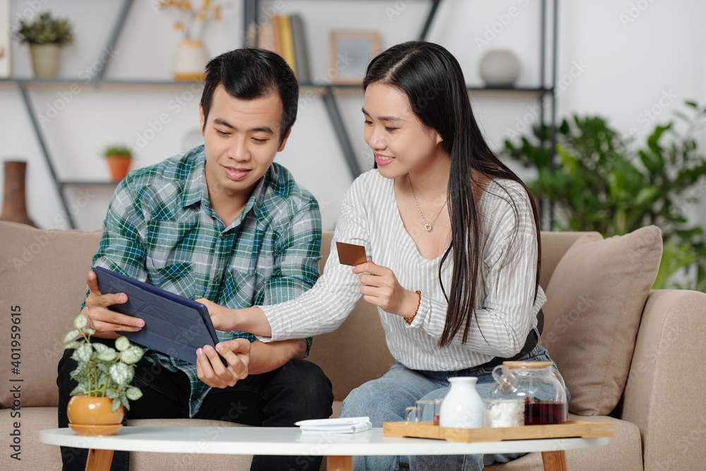 Cheerful young Vietnamese couple with credit card and digital tablet making purchases online