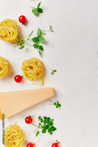 Ingredients for cooking pasta - tagliatelle, tomato, garlic, basil, parmesan cheese on white wooden background flat lay, top view, frame, copy space, Italian food concept.