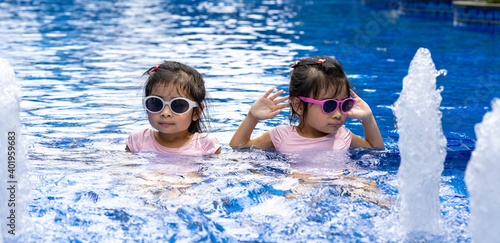 Portrait of pretty asian twins smilling and posing on swimming pool background wearing pink swim suit and sun glasses