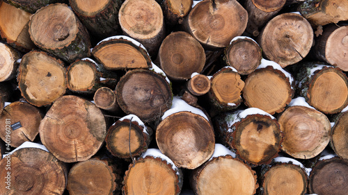 Stacked wooden sawn logs covered with snow and laid out in several rows. Wooden natural background. Close up view of firewood.