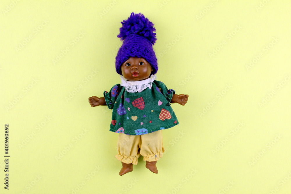 Little doll in a knitted hat. Doll toy for child play on yellow background Little doll in a knitted hat. Doll toy for child play on yellow background