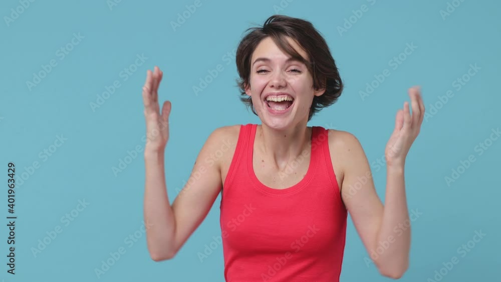 Side view of surprised young woman 20s in pink tank top isolated on blue background studio. People lifestyle concept. Turns around camera say wow spreading hands doing winner gesture showing thumbs up Side view of surprised young woman 20s in pink tank top isolated on blue background studio. People lifestyle concept. Turns around camera say wow spreading hands doing winner gesture showing thumbs up