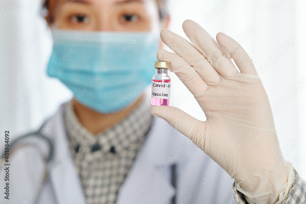 Young female general practitioner in medical mask and latex gloves showing covid-19 vaccine Young female general practitioner in medical mask and latex gloves showing covid-19 vaccine