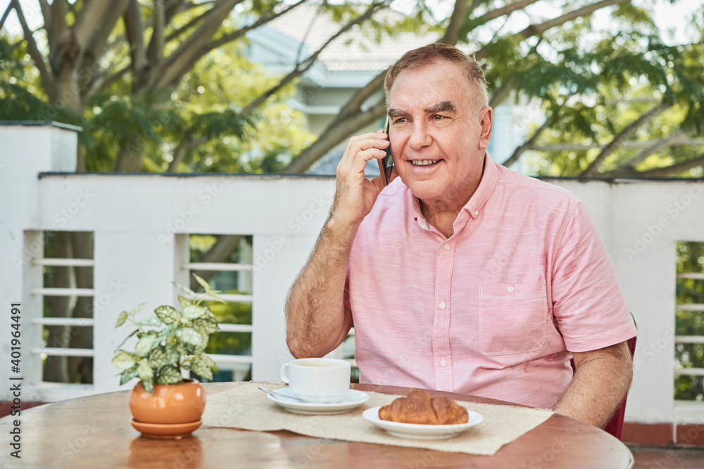 Positive senior man eating breakfast in outdoor cafe and talking on phone with friend or family memeber Positive senior man eating breakfast in outdoor cafe and talking on phone with friend or family memeber