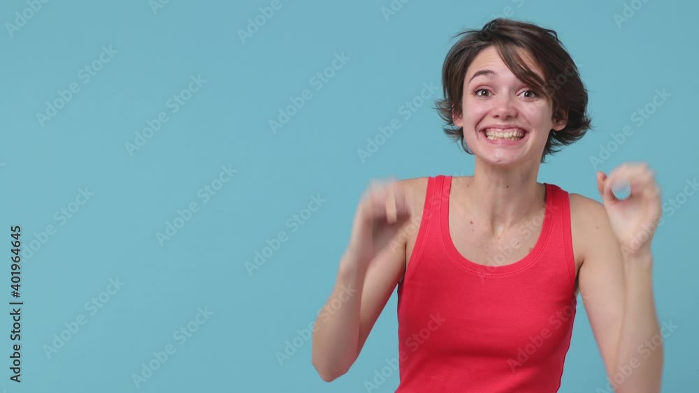 Surprised young brunette woman 20s in pink tank top posing isolated on pastel blue color background in studio. People lifestyle concept. Pointing index finger aside showing thumb up ok okay gesture Surprised young brunette woman 20s in pink tank top posing isolated on pastel blue color background in studio. People lifestyle concept. Pointing index finger aside showing thumb up ok okay gesture
