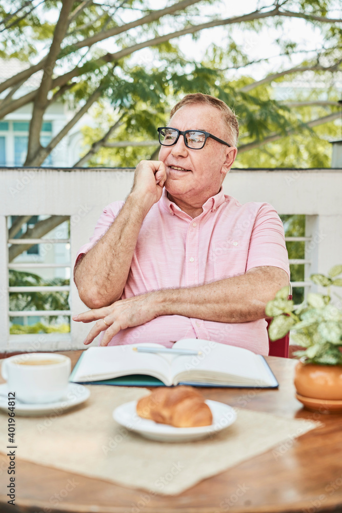 Portrait of pensive smiling senior man eating breakfast and filling journal with thoughts and ideas Portrait of pensive smiling senior man eating breakfast and filling journal with thoughts and ideas