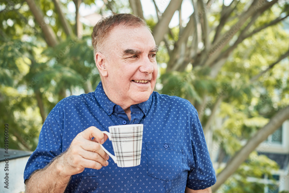 Portrait of smiling senior man standing outdoors with mug of coffee and looking away