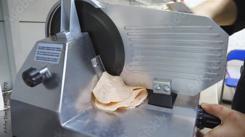 Close up arm of cook chopping sausage on electric food slicer at kitchen. Male hand of chef using cutting machine for ham at cuisine restaurant. Process to prepare ingredients for cooking pizza