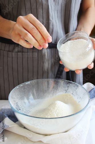 Household. The hands of a housewife add the ingredients to a bowl of flour for kneading the dough. Family celebration.