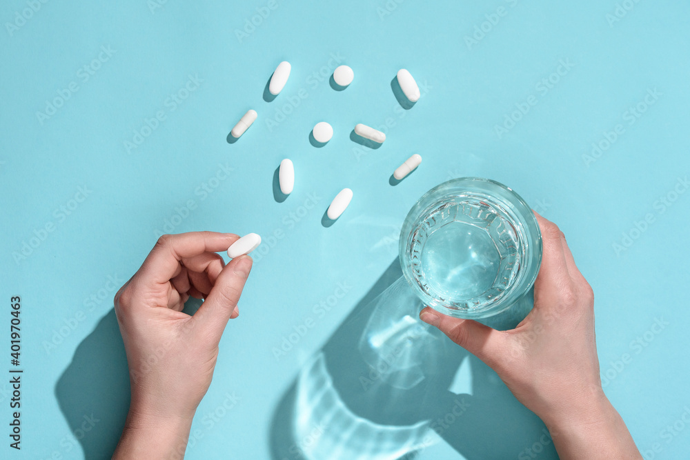 Φωτογραφία Woman holding in hands white medical pill and glass of water on light blue background, copy space