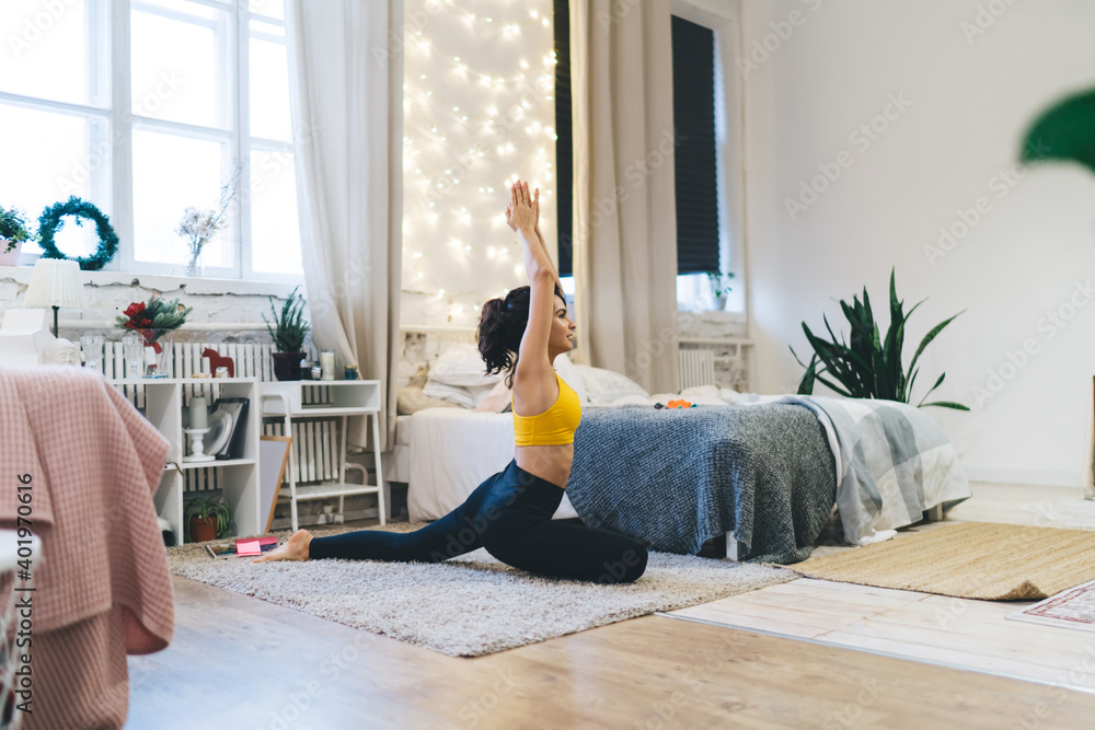 Flexible female yogi practicing hatha at rug stretching body muscles for keeping perfect slim figure, Caucasian fit girl enjoying harmony inspiration during pilates training in cosy home interior