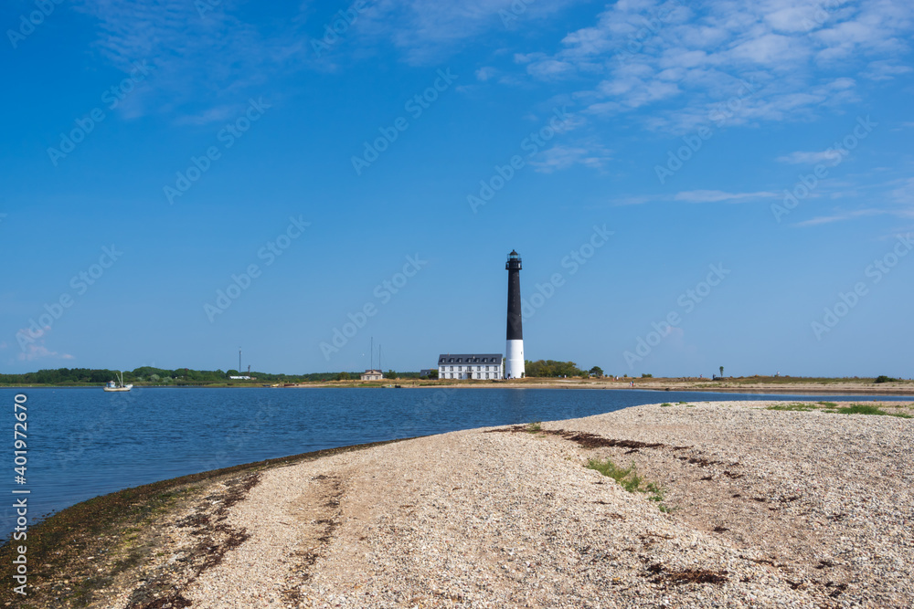 View to the beach of Sõrve peninsula cape with sand and pebbles by coastline. Lighthouse in the background. Focus on water and pebbles in foreground
