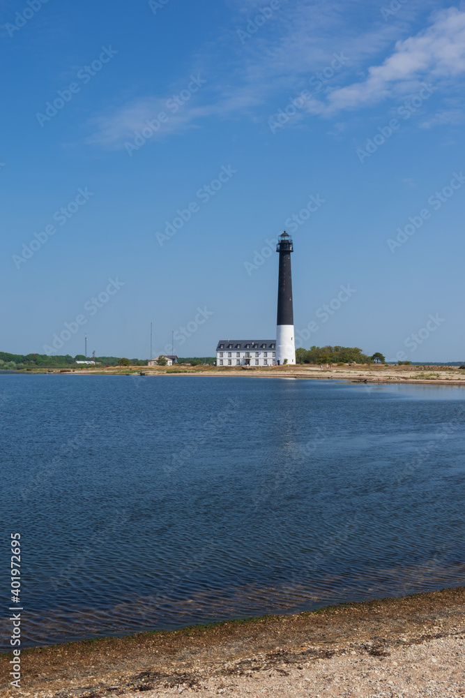 
View to the beach of Sõrve peninsula cape with sand and pebbles by coastline. Lighthouse in the background. Focus on water and pebbles in foreground
