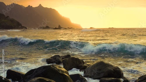Ocean waves crash on rocks and spray in beautiful sunset light near Playa de Benijo beach in Tenerife Canary Islands