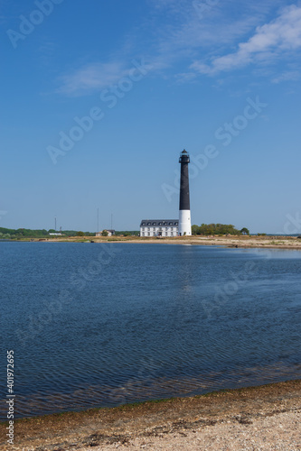  View to the beach of Sõrve peninsula cape with sand and pebbles by coastline. Lighthouse in the background. Focus on water and pebbles in foreground 