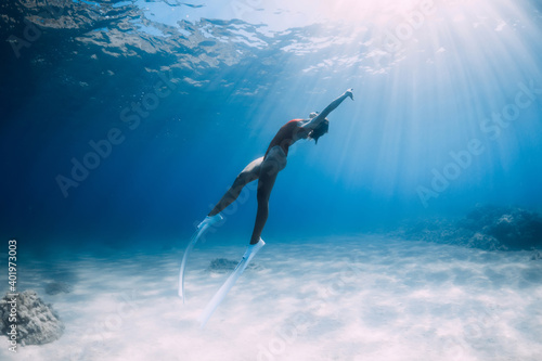 Freediver girl glides over sandy sea with white fins. Freediving with attractive woman in clear ocean
