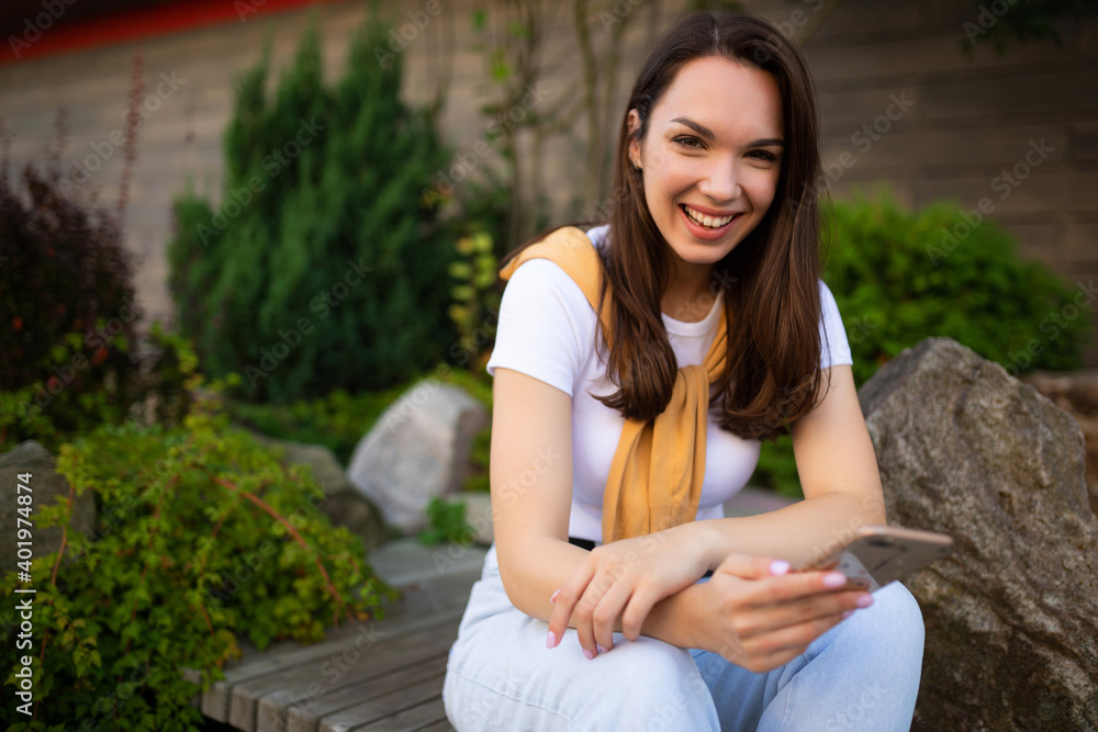 young woman freelancer sits in the park and enjoys a coffee break with a phone in her hands young woman freelancer sits in the park and enjoys a coffee break with a phone in her hands