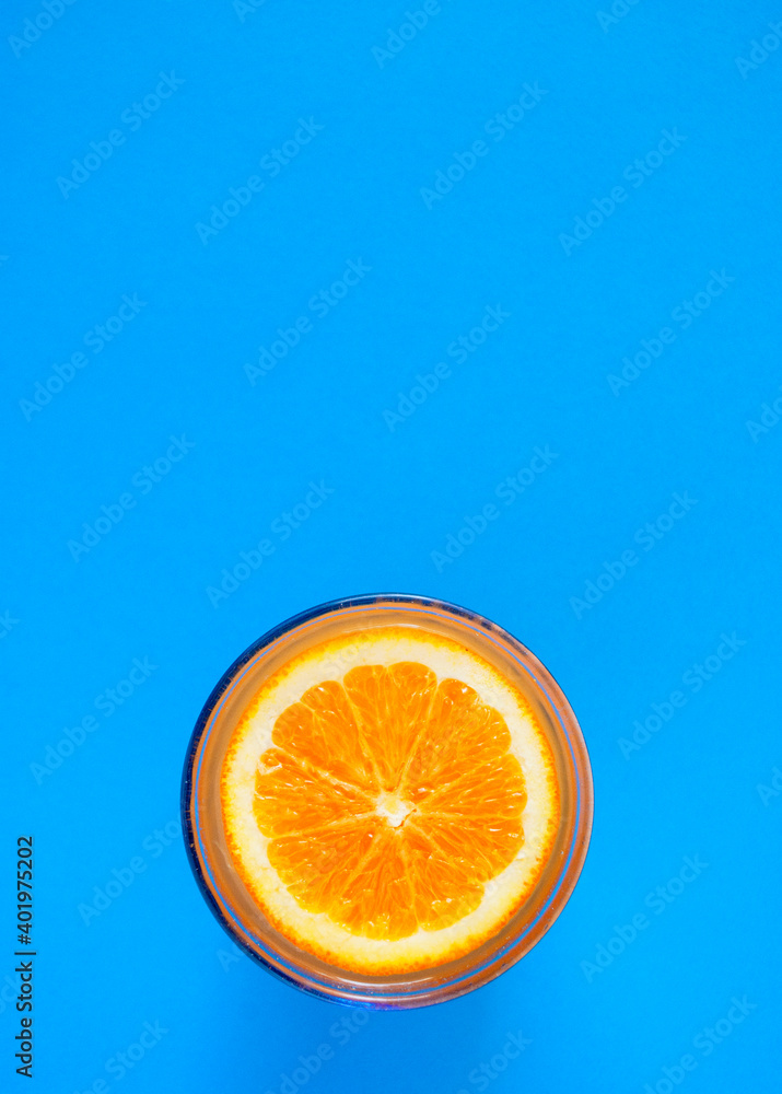Cut orange on the surface of orange juice in a glass on a blue background. Cut orange on the surface of orange juice in a glass on a blue background.