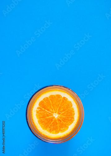 Cut orange on the surface of orange juice in a glass on a blue background.