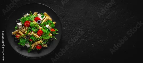 Panel kuchenny z motywem Salad with pasta, arugula, tomato, cheese and olives on black plate on Dark grey black slate background
