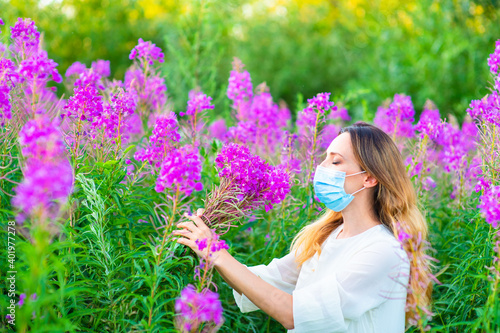 Φωτογραφία A girl in a medical mask sniffs a bouquet of purple flowers in her hands