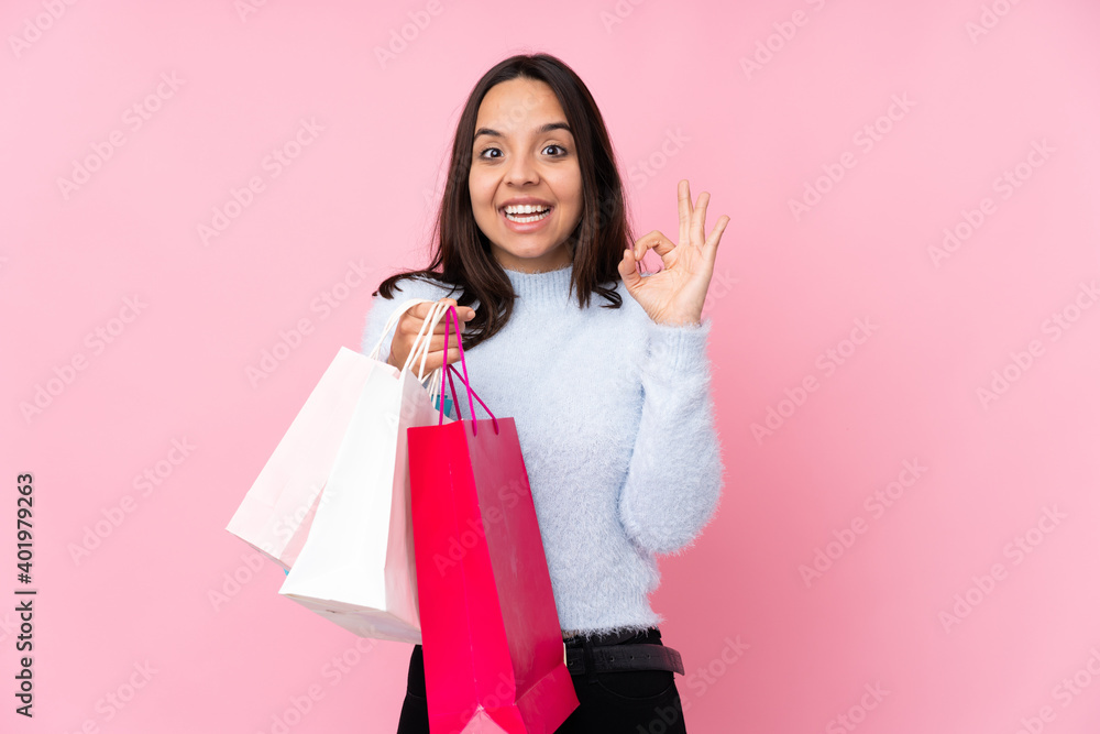 Young woman with shopping bag over isolated pink background surprised and showing ok sign