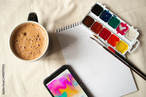 Set of watercolor paints, scetchbook, paintbrush and a cup of coffee for breakfast. photo