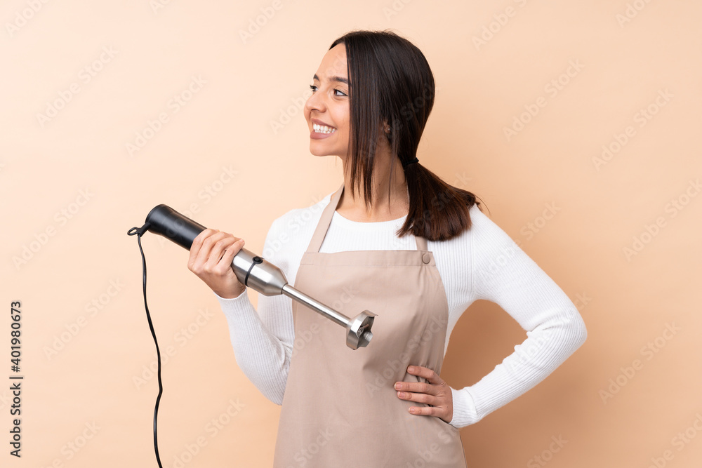 Young brunette girl using hand blender over isolated background looking side Young brunette girl using hand blender over isolated background looking side