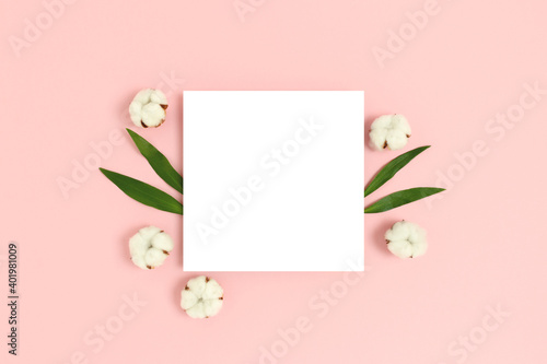 Square paper card mockup with frame made of cotton and green leaves on a pink pastel background. Eco concept.