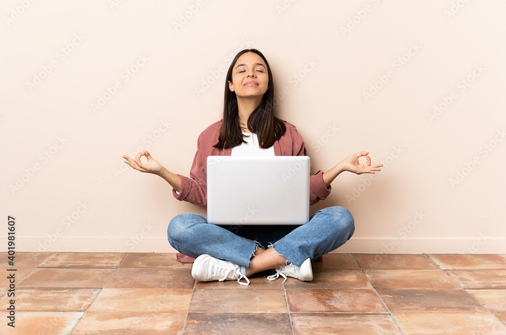 Young mixed race woman with a laptop sitting on the floor in zen pose Young mixed race woman with a laptop sitting on the floor in zen pose