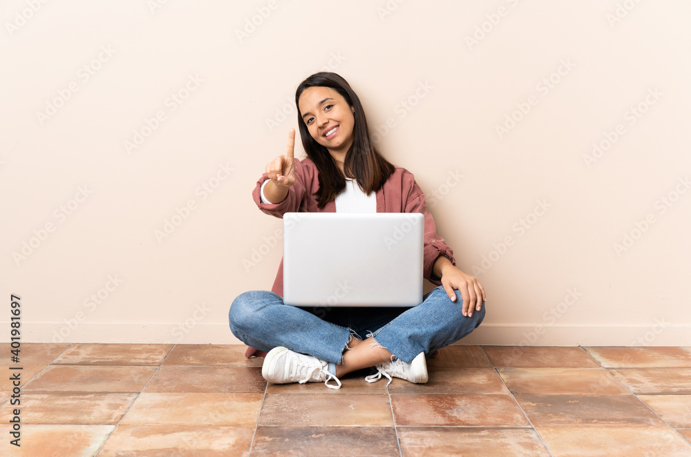 Young mixed race woman with a laptop sitting on the floor showing and lifting a finger Young mixed race woman with a laptop sitting on the floor showing and lifting a finger