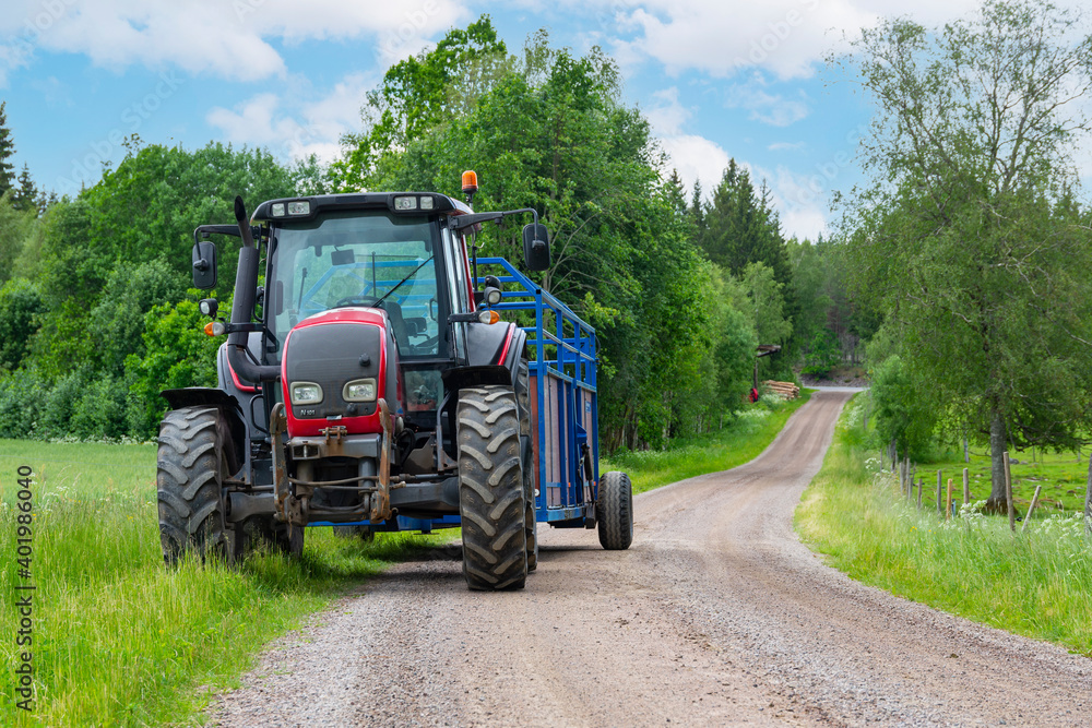 Tractor And Trailer standing near the road in farm during harvesting work in summer under sky with clouds near forest Tractor And Trailer standing near the road in farm during harvesting work in summer under sky with clouds near forest
